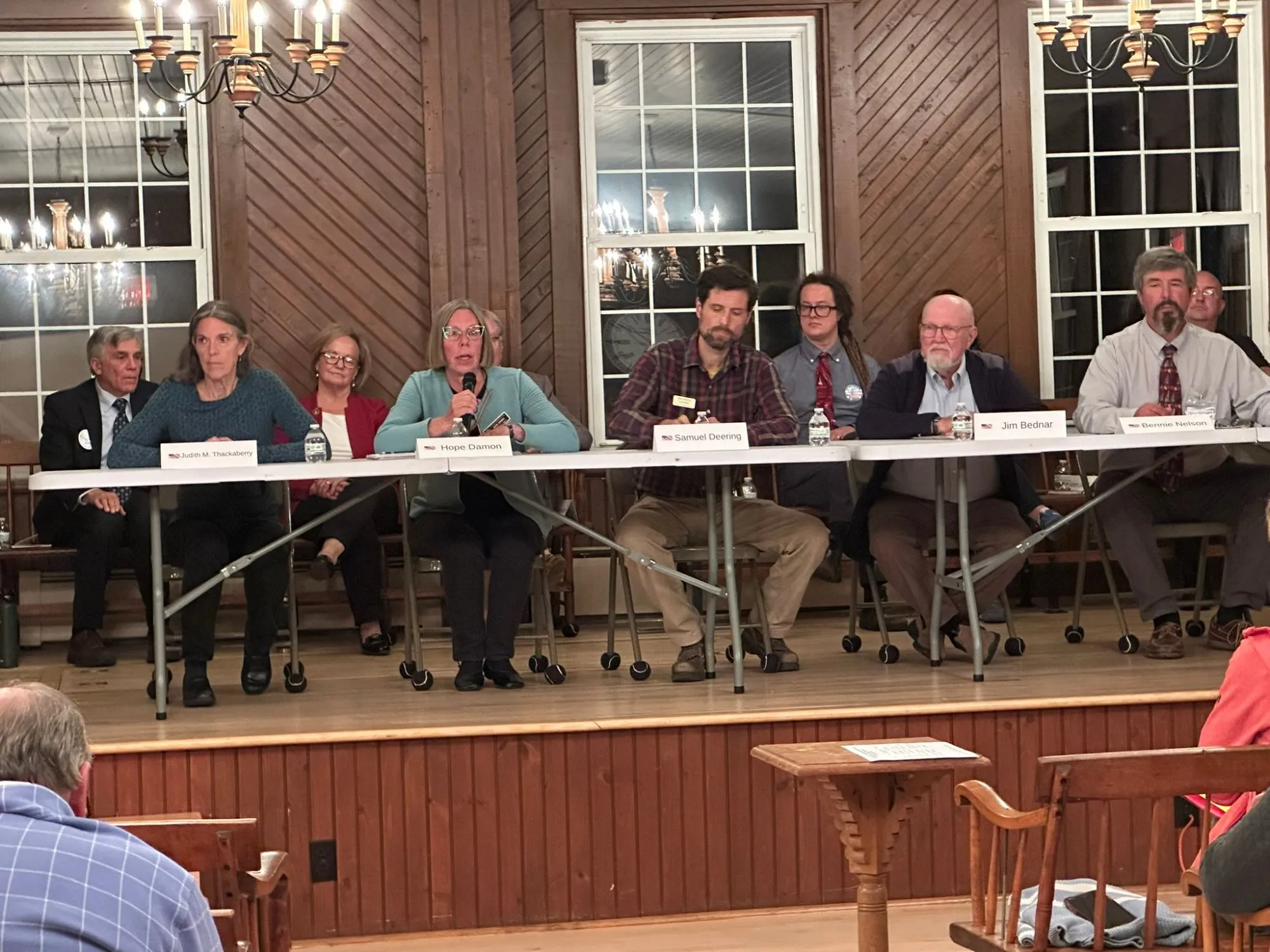 Jim Bednar seated behind his name placard with other candidates at the forum table as one of them answers a question